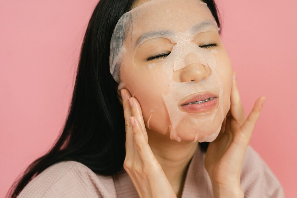 Asian woman applying a hydrating facial sheet mask for skincare routine therapy.
